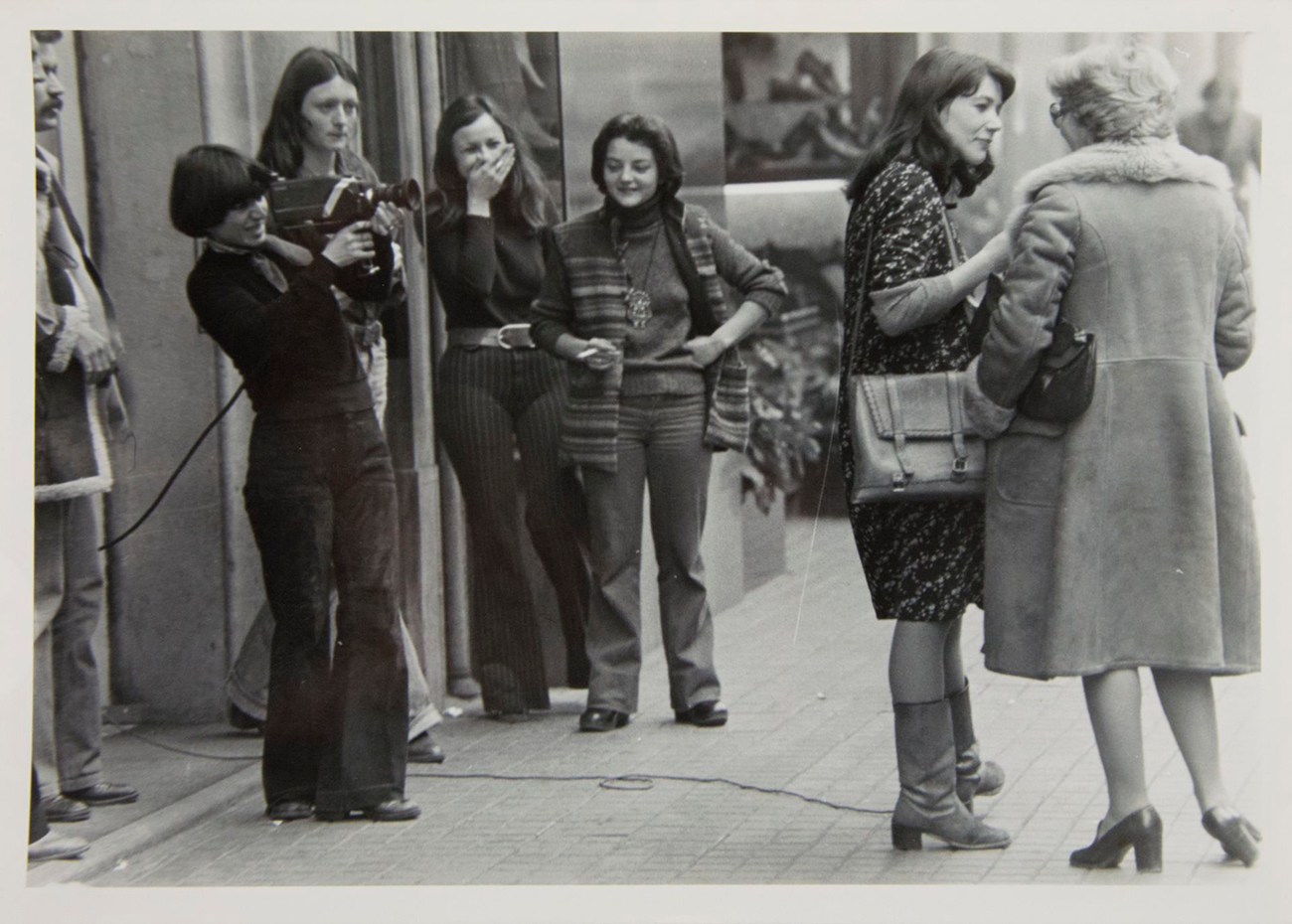 Fotografia d'una entrevista a una dona al carrer amb un equip de vídeo i joves rient i observant l'acció, Video-Nou, 1977