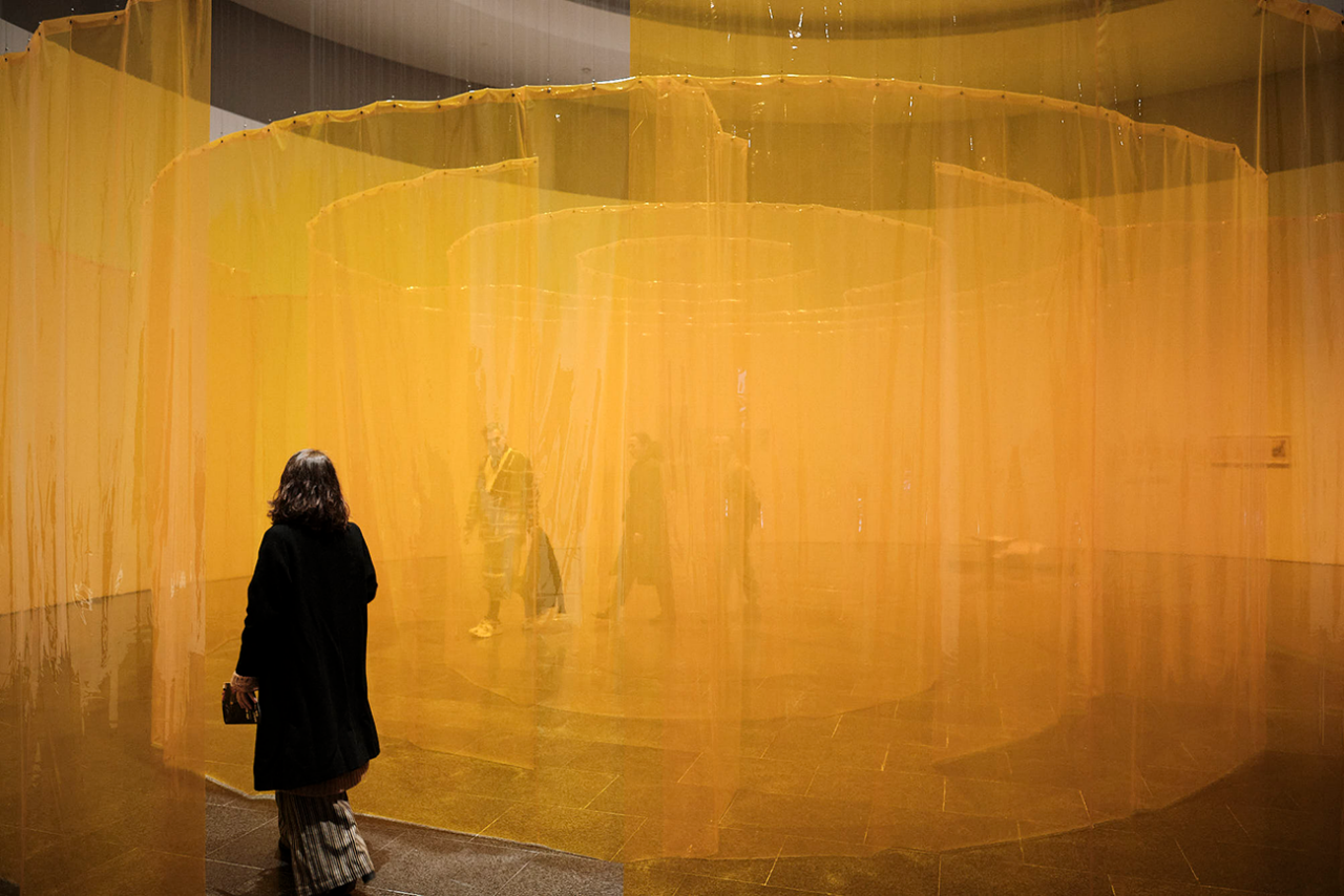 A woman observes an art installation consisting of a labyrinth of translucent yellow plastic.