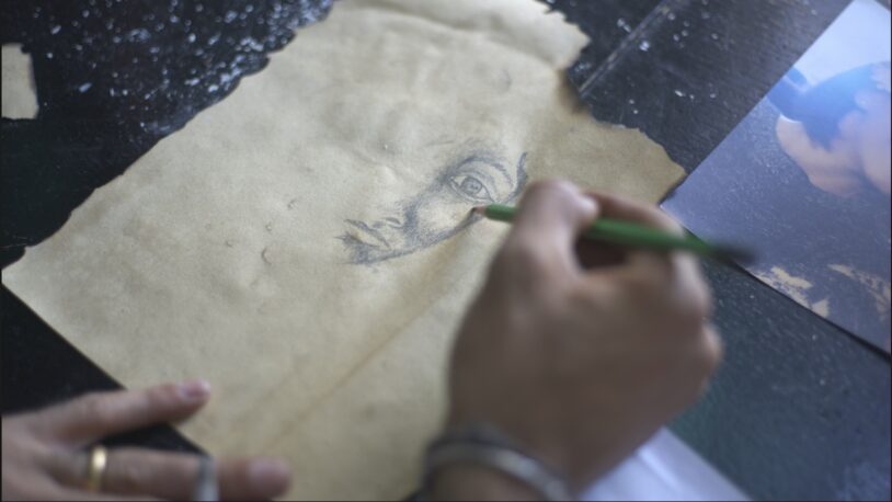 Les mans d'un artista tracen amb llapis el costat dret del retrat d'un home empresonat.