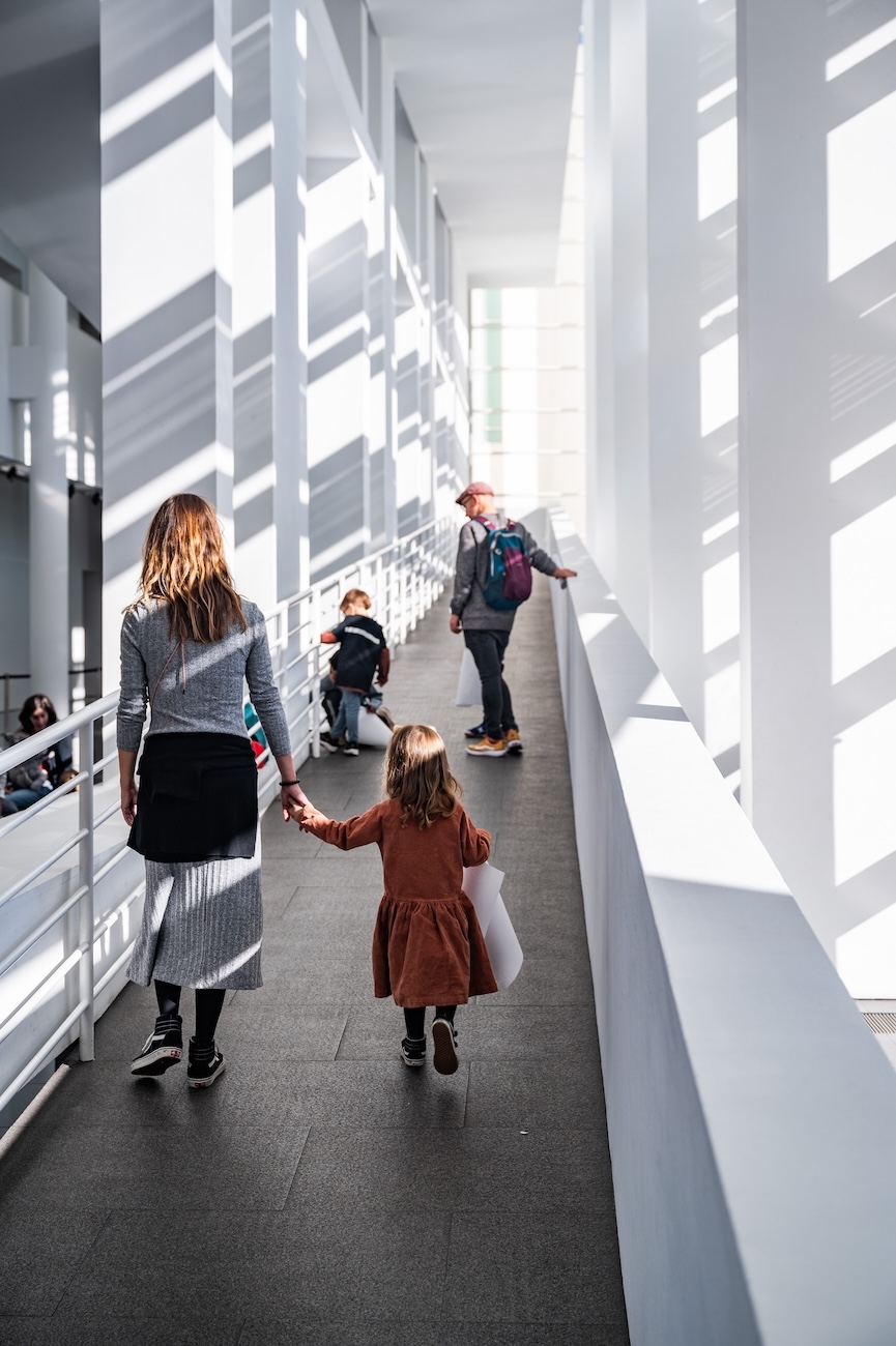 A woman and a girl walk hand in hand along a ramp at the MACBA. In the background, a man and three children are in the same space.