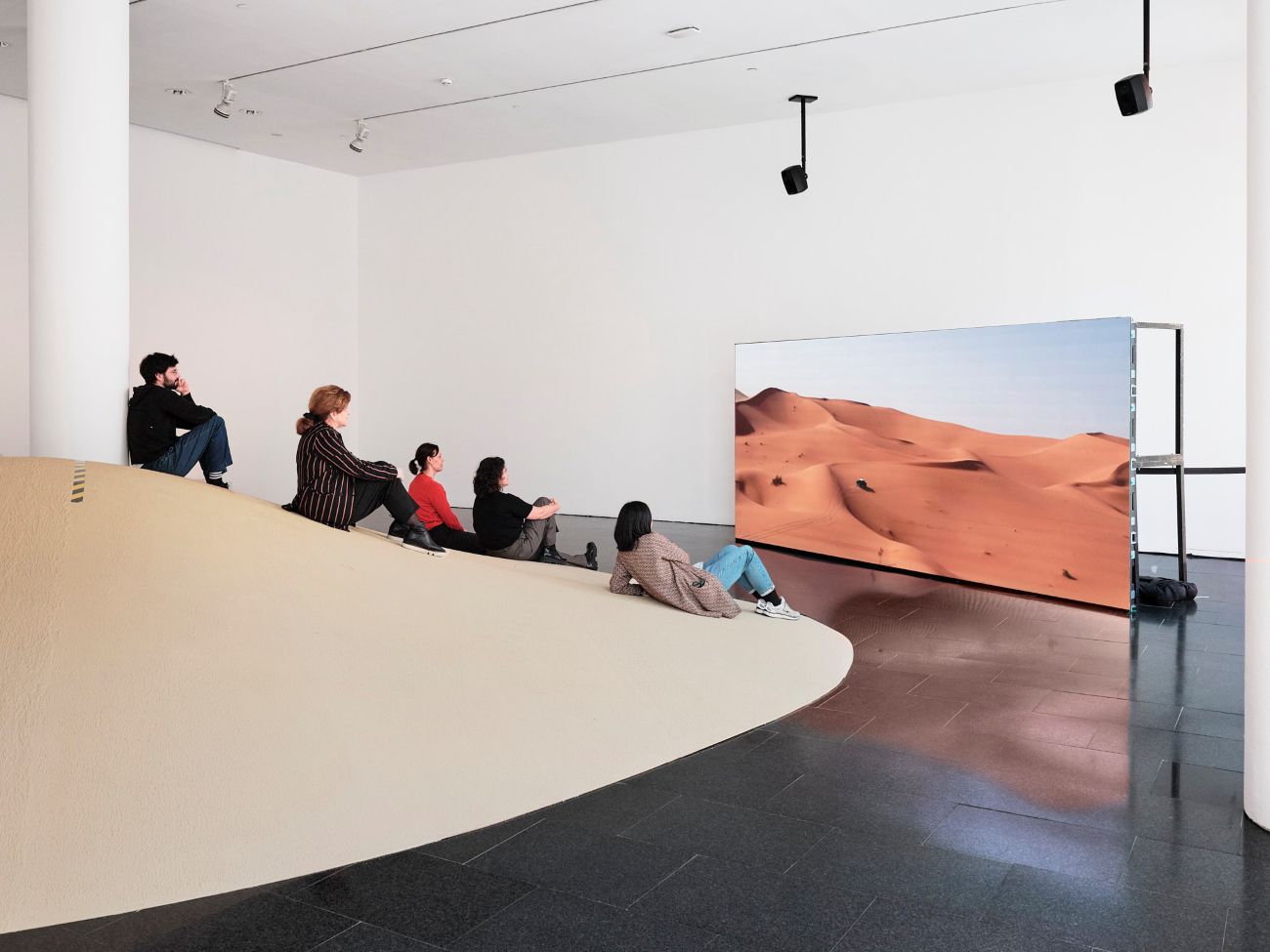 Grup de visitants asseguts sobre la duna artificial, contemplant el documental La Tercera Torsió projectat en una pantalla de gran format.