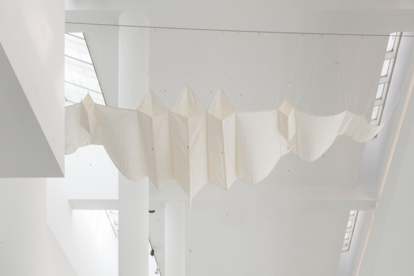 Escultura textil blanca de gran formato suspendida del techo del museo en forma de pájaro cometa.