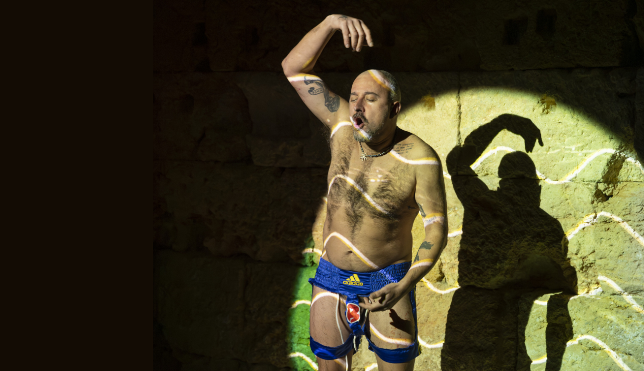 Marc Vives apareix il·luminat per un focus teatral que contrasta amb la foscor de l'escenari. Amb el tors nu, porta unes bermudes retallades com si fossin un taparrabos amb lliga. Amb els ulls tancats, i la boca oberta, té un braç elevat per sobre del cap amb la mà corbada, mentre que l'altra mà se situa a prop del seu abdomen.