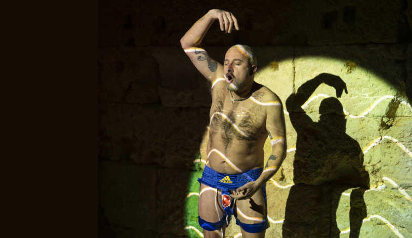 Marc Vives apareix il·luminat per un focus teatral que contrasta amb la foscor de l'escenari. Amb el tors nu, porta unes bermudes retallades com si fossin un taparrabos amb lliga. Amb els ulls tancats, i la boca oberta, té un braç elevat per sobre del cap amb la mà corbada, mentre que l'altra mà se situa a prop del seu abdomen.