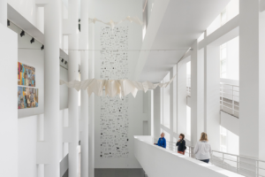 Tres persones a la rampa del MACBA observen una escultura tèxtil blanca suspesa del sostre en forma de ocell-estel.