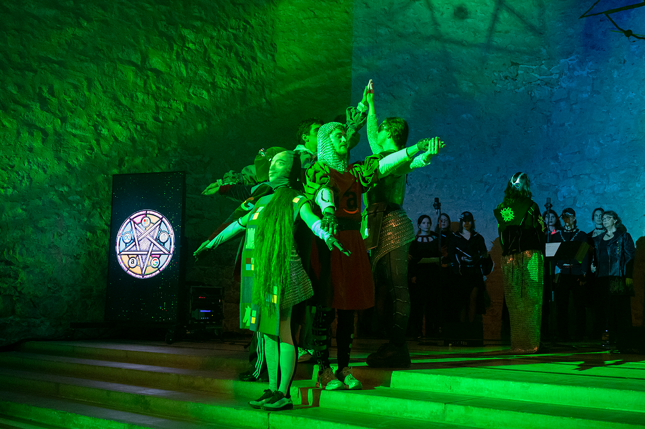 Cor de persones cantant amb altres participants al voltant actuant, sobre un fons de colors amb pantalles de suport.